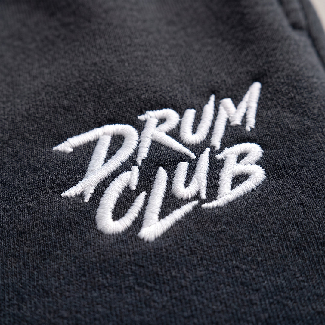 Close-up of a dark charcoal gray fabric with white embroidered text reading 'DRUM CLUB'.