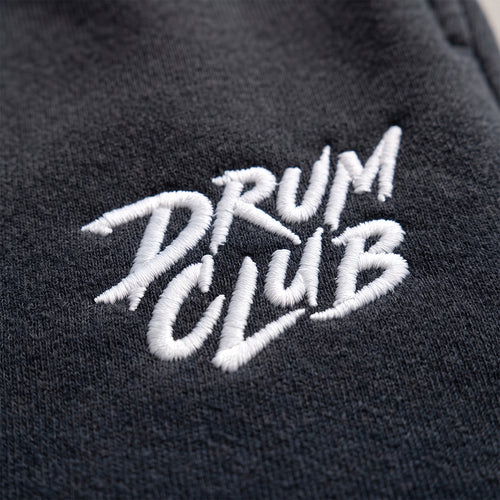 Close-up of a dark charcoal gray fabric with white embroidered text reading 'DRUM CLUB'.